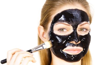 Siyah detoks detoks ile uygulanan genç bir kadın maskesini yüzüne doğru sıyırdı. Deriyle ilgilenen bir kız. Güzellik tedavisi. Cilt bakımı.