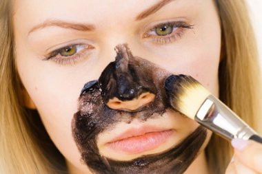 Genç bir kadın yüzünde siyah detoks çamuruyla fırça kömür maskesi takıyor. Yağlı ciltle ilgilenen bir kız. Güzellik tedavisi. Cilt bakımı.