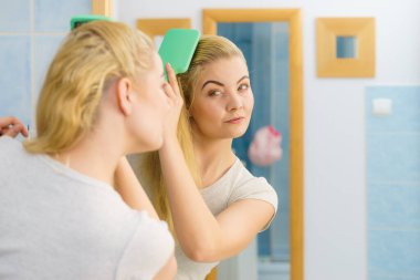 Saçını fırçayla tarayan mutlu kadın. Genç, gülümseyen, doğal sarışın, uzun saçlı bir kadın sabah duşundan sonra banyoda..