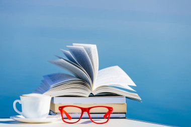 Tatilde okumak. Kahve fincanı, kitap ve kırmızı bardaklar mavi deniz suyuna karşı. Tatil gezisinde dinlenmek. Zihinsel sağlık sorunları.