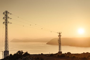 Elektrik iletim direkleriyle kıyı şeridi, elektrik hatları yüksek voltaj kuleleri. İspanya 'da günbatımı manzarası