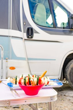 Izgarada kızartılmaya hazır çeşit çeşit lezzetli sebze şişleri. Barbekü yemeği dışarıda. Arka planda karavan var..