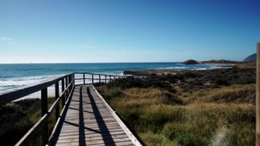 Sahil manzarası, deniz suyuna giden ahşap yolu olan kayalık deniz kıyısı. Cala Magre Sahili, Calique Bölgesel Parkı, Murcia Bölgesi İspanya.