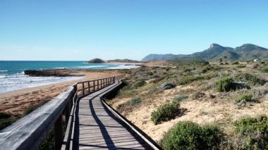 Sahil manzarası, deniz suyuna giden ahşap yolu olan kayalık deniz kıyısı. Cala Magre Sahili, Calique Bölgesel Parkı, Murcia Bölgesi İspanya.