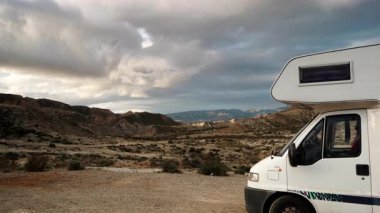 Dağların üzerinde hareket eden tüylü bulutlar ve Tabernas Çölü, Almerya Bölgesi, Endülüs İspanya 'da kamp yapan karavan aracı..