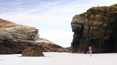 Kameralı bir kadın, Kuzey İspanya 'nın Lugo, Galiçya eyaletindeki katedrallerin plajlarını, playa las kategorilerini ziyaret ediyor. Turistler uçurum oluşumlarından seyahat fotoğrafları çekerler..