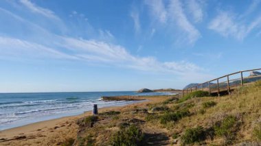 Sahil manzarası, denize giden ahşap yolu olan deniz kıyısı, dalgalar ağır çekimde hareket ediyor. Cala Magre Sahili, Calique Bölgesel Parkı, Murcia Bölgesi İspanya.