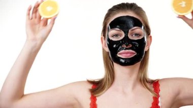 Yüzünde karbonhidrat maskesi olan genç bir kadın elinde turuncu meyve yarımları, gözleri kaplayan beyaz bir kadın. Güzellik tedavisi. Cilt bakımı.