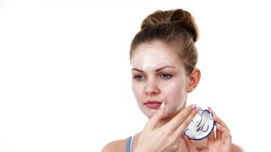 Maske takan genç bir kadın yüzüne nemlendirici krem sürüyor. Cilt nemlendiricisine dikkat eden bir kız. Cilt bakımı.