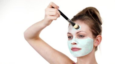 Yüzüne yeşil çamur maskesi dayayan genç bir kadın. Genç kız yağlı cildiyle ilgileniyor, gözenekleri temizliyor. Güzellik tedavisi. Cilt bakımı.