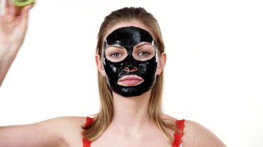 Yüzünde karbonhidrat maskesi olan genç bir kadın elinde kivi meyve yarımları, gözleri kaplayan beyaz bir kadın. Güzellik tedavisi. Cilt bakımı.