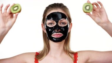 Yüzünde karbonhidrat maskesi olan genç bir kadın elinde kivi meyve yarımları, gözleri kaplayan beyaz bir kadın. Güzellik tedavisi. Cilt bakımı.