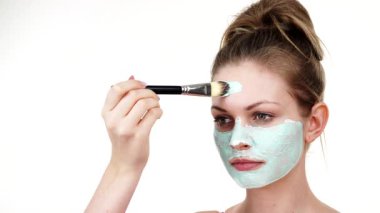 Yüzüne yeşil çamur maskesi dayayan genç bir kadın. Genç kız yağlı cildiyle ilgileniyor, gözenekleri temizliyor. Güzellik tedavisi. Cilt bakımı.