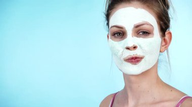 Yüzünde beyaz kuru çamur maskesi olan genç bir kadın, maviliğe karşı. Genç kız yağlı cildiyle ilgileniyor, gözenekleri temizliyor. Güzellik tedavisi. Cilt bakımı.