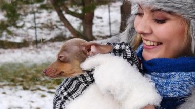 Köpeğiyle oynayan genç bir kadın, pinscher ratter prazsky krysarik, kış havasında dışarıda. Dişi köpek yavrusuna sevgiyle sarılıyor..