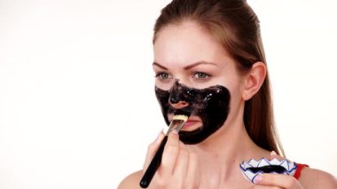 Genç bir kadın yüzüne karbonhidrat temizleme maskesi takıyor, yüzüne, beyaza. Genç kız yağlı cildiyle ilgileniyor, gözenekleri temizliyor. Güzellik tedavisi. Cilt bakımı.