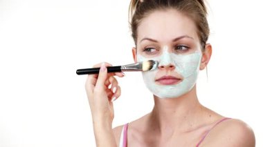 Yüzüne yeşil çamur maskesi dayayan genç bir kadın. Genç kız yağlı cildiyle ilgileniyor, gözenekleri temizliyor. Güzellik tedavisi. Cilt bakımı.