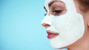 Yüzünde beyaz kuru çamur maskesi olan genç bir kadın, maviliğe karşı. Genç kız yağlı cildiyle ilgileniyor, gözenekleri temizliyor. Güzellik tedavisi. Cilt bakımı.