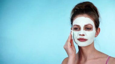 Yüzünde beyaz kurumuş çamur maskesi olan genç bir kadın pamuklu çubukla maviden temizleniyor. Yağlı ciltle ilgilenen genç bir kız. Güzellik tedavisi. Cilt bakımı.