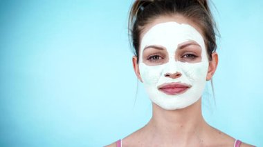 Yüzünde beyaz kuru çamur maskesi olan genç bir kadın, maviliğe karşı. Genç kız yağlı cildiyle ilgileniyor, gözenekleri temizliyor. Güzellik tedavisi. Cilt bakımı.