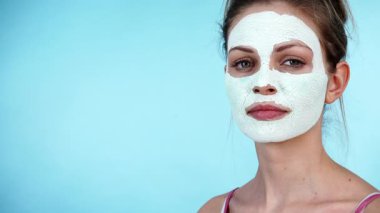 Yüzünde beyaz kuru çamur maskesi olan genç bir kadın, maviliğe karşı. Genç kız yağlı cildiyle ilgileniyor, gözenekleri temizliyor. Güzellik tedavisi. Cilt bakımı.
