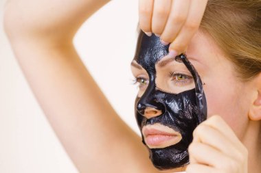 Karbonhidratlı siyah maskesini yüzünden, beyazın üstüne çıkaran genç bir kadın. Genç kız yağlı cildiyle ilgileniyor, gözenekleri temizliyor. Güzellik tedavisi. Cilt bakımı.