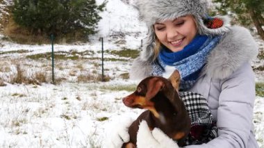 Genç bir kadın kış havasında yavru köpeğiyle dışarıda oynuyor..