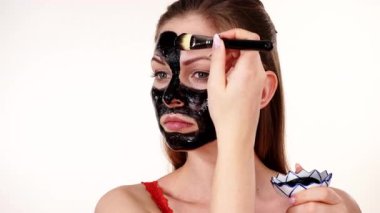 Genç bir kadın yüzüne karbonhidrat temizleme maskesi takıyor, yüzüne, beyaza. Genç kız yağlı cildiyle ilgileniyor, gözenekleri temizliyor. Güzellik tedavisi. Cilt bakımı.