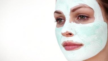 Yüzünde beyaz yeşil çamur maskesi olan genç bir kadın. Genç kız yağlı cildiyle ilgileniyor, gözenekleri temizliyor. Güzellik tedavisi. Cilt bakımı.