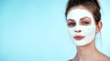 Yüzünde beyaz kuru çamur maskesi olan genç bir kadın, maviliğe karşı. Genç kız yağlı cildiyle ilgileniyor, gözenekleri temizliyor. Güzellik tedavisi. Cilt bakımı.