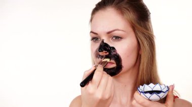 Genç bir kadın yüzüne karbonhidrat temizleme maskesi takıyor, yüzüne, beyaza. Genç kız yağlı cildiyle ilgileniyor, gözenekleri temizliyor. Güzellik tedavisi. Cilt bakımı.