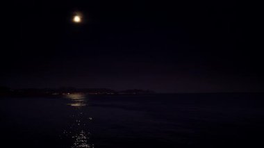 Gece dolunayda, kara gökyüzünde, kıyı bölgesinde. Ay ışığı suya yansıyor.