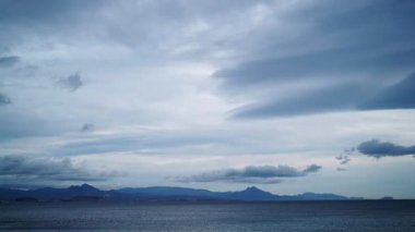 Sakin deniz suyunun üzerinde hareket eden bulutların hızlanması, bulutlu bir gün. Ufuktaki tepe kıyı şeridi.