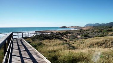Sahil manzarası, deniz suyuna giden ahşap yolu olan kayalık deniz kıyısı. Cala Magre Sahili, Calique Bölgesel Parkı, Murcia Bölgesi İspanya.