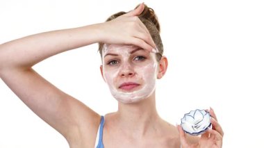 Maske takan genç bir kadın yüzüne nemlendirici krem sürüyor. Cilt nemlendiricisine dikkat eden bir kız. Cilt bakımı.