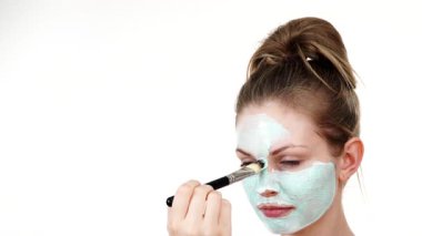 Yüzüne yeşil çamur maskesi dayayan genç bir kadın. Genç kız yağlı cildiyle ilgileniyor, gözenekleri temizliyor. Güzellik tedavisi. Cilt bakımı.