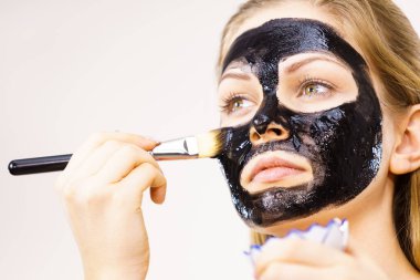 Yüzüne siyah detoks çamur maskesi süren genç bir kadın. Deriyle ilgilenen bir kız. Güzellik tedavisi. Cilt bakımı.