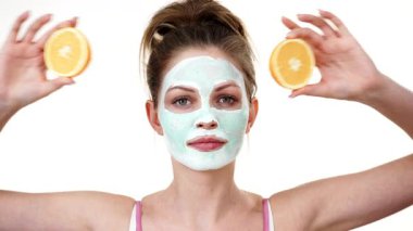 Yüzünde beyaz yeşil çamur maskesi olan genç kadın, turuncu meyve yarısını tutan, gözleri kapsayan. Genç kız cilt bakımı. Güzellik tedavisi.