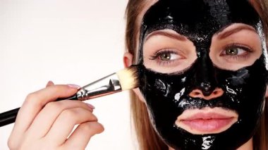 Genç bir kadın yüzüne karbonhidrat temizleme maskesi takıyor, yüzüne, beyaza. Genç kız yağlı cildiyle ilgileniyor, gözenekleri temizliyor. Güzellik tedavisi. Cilt bakımı.