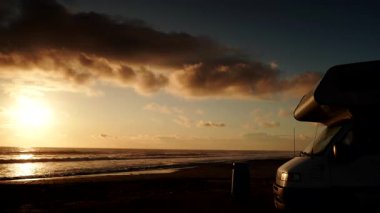 Kamp aracı, İspanya 'da güneş doğarken plajda kamp yapıyor. Karavan tatili. Bulutlar gökyüzünde hareket ediyor. Zaman aşımı