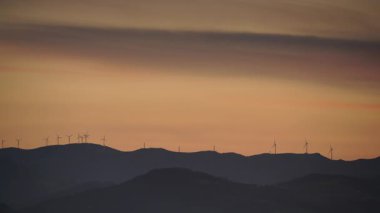 Akşam manzarası. Gün batımında tepede rüzgâr türbinleri çiftliği.