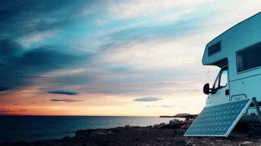 Gün batımında bulutların hızla hareket etmesi deniz kıyısındaki taşınabilir güneş paneli ve karavan aracının üzerinden geçiyor. Kervan tatilinde yenilenebilir enerji.