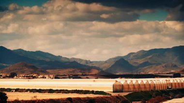 İspanya kıyılarında büyük ticari cam seralar ile hareket eden bulutların zaman akışı. Endüstriyel tarım. Murcia bölgesi, İspanya.