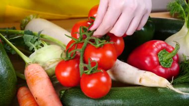 Diğer sebzelerin önünde bitkinin üzerinde kiraz domateslerini gösteren tanınmamış bir kadın eli. Sağlıklı yeme kavramı.