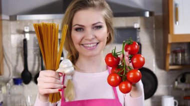 Komik kadın elinde uzun makarna ve taze domatesle spagetti pişirmeyi düşünüyor..