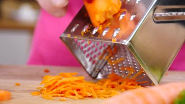 Kadının el rendeleyici havucu mutfak tahtasında yavaş çekimde sebze rendesi kullanarak yakın çekim..