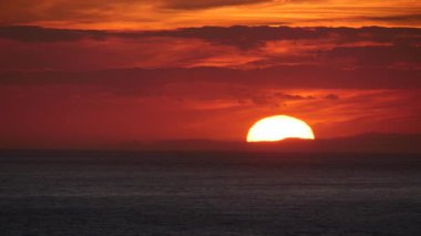 Deniz üzerinde gün batımında kızıl gökyüzü. Güneş ufukta batıyor. Akşam doğa manzarası.