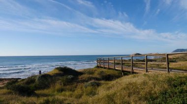 Sahil manzarası, denize giden ahşap yolu olan deniz kıyısı, dalgalar ağır çekimde hareket ediyor. Cala Magre Sahili, Calique Bölgesel Parkı, Murcia Bölgesi İspanya.