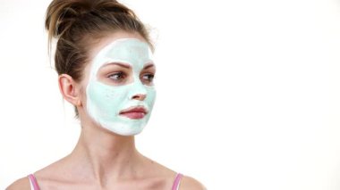 Yüzünde beyaz yeşil çamur maskesi olan genç bir kadın. Genç kız yağlı cildiyle ilgileniyor, gözenekleri temizliyor. Güzellik tedavisi. Cilt bakımı.