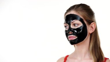 Yüzünde karbonhidrat maskesi olan genç bir kadın kameraya ve yana, beyaza bakıyor. Güzellik tedavisi. Cilt bakımı.